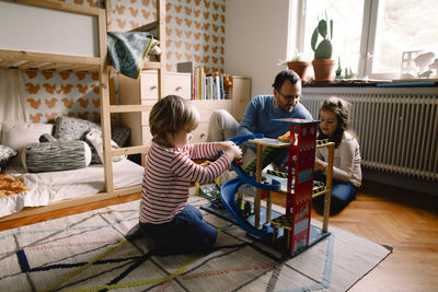 Girl playing with toy cars while father and sister talking in bedroom at home