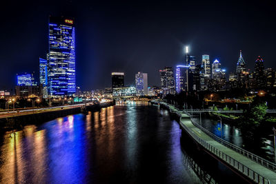 Illuminated buildings by river against sky at night