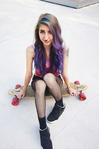 Portrait of young woman sitting on skateboard at park