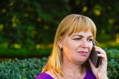 Close-up caucasian blond woman talking, speaking on the phone outside, outdoor. 40s years old woman