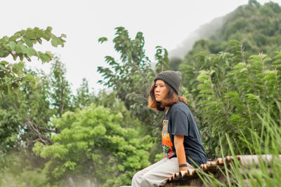 Side view of young man standing against trees