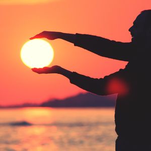 Optical illusion of man holding sun during sunset