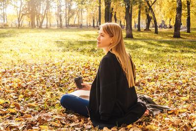 Woman using laptop while sitting on leaves in park