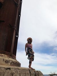 Low angle view of woman standing by built structure against sky