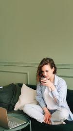 Young woman using laptop while sitting on sofa at home