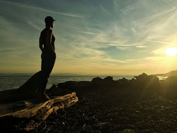 Man standing on rock by sea against sky during sunset