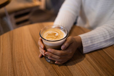 Hand holding hot aromatic cappuccino in cafe