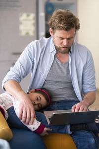 Businessman taking care of girl while using laptop at home