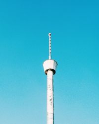 Low angle view of communications tower and building against clear blue sky