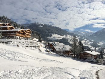 Houses on snow covered field by mountains against cloudy sky