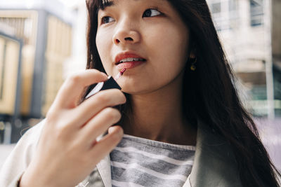 Young woman with long hair applying lip gloss