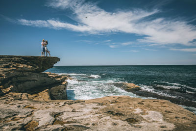 Couple on rock by sea against sky
