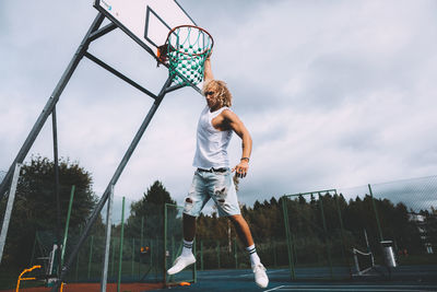 Low angle view of boy playing basketball against sky