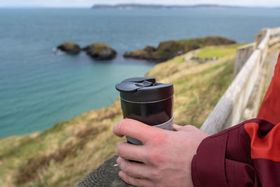 Midsection of person holding sunglasses on sea shore