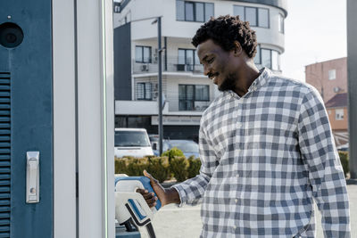 Smiling young man holding car charger at station