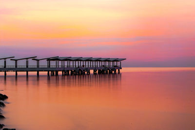 Pier on sea against orange sky