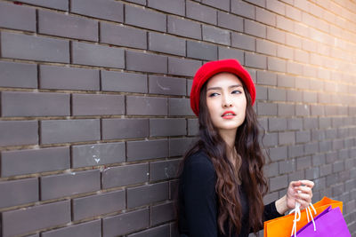 Portrait of young woman looking away against wall