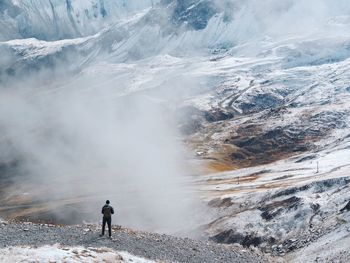 Rear view of man standing on mountain during foggy weather