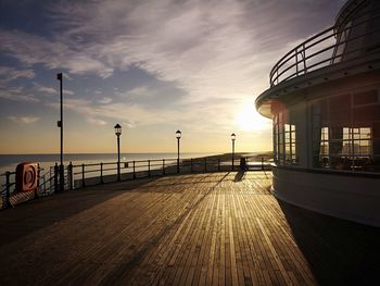 Empty footpath by sea against sky during sunset