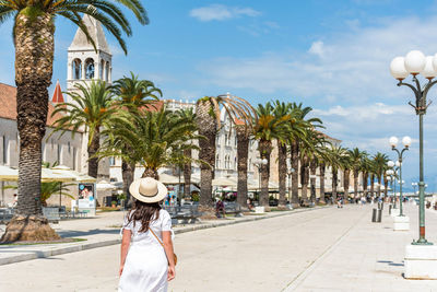 Rear view of woman wearing white sundress, walking on waterfront promenade in trogir, croatia