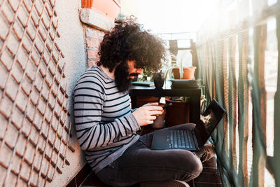 Side view of man using mobile phone while sitting in balcony