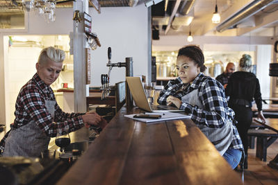 Woman using laptop while standing by partner at bar counter