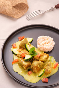 Lamb curry with currysauce courgettes and tomatoes on a black plate