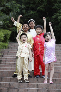 Portrait of cute friends with hand raised in traditional clothing sitting on steps