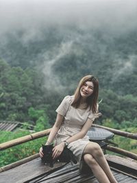 Young woman sitting on railing against mountain