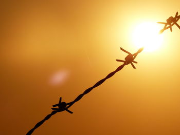 Close-up of silhouette electric wire fence against sky during sunset