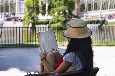 Side view of woman reading book while sitting on bench in city