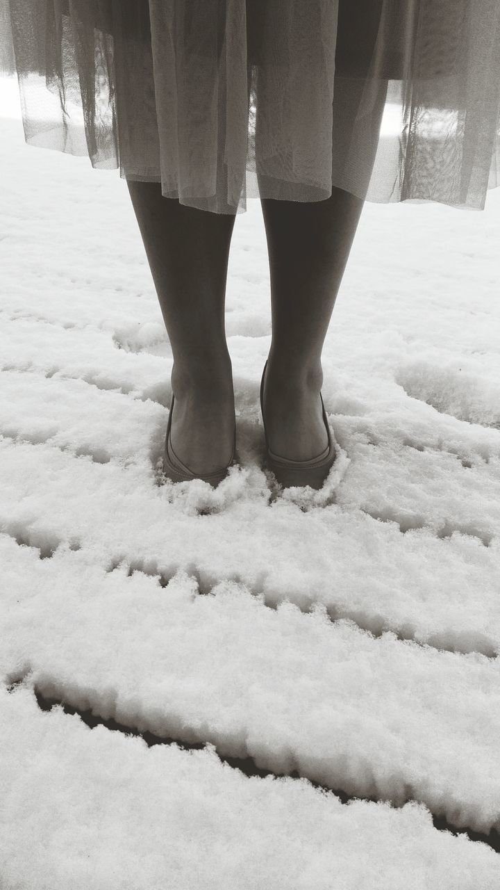 LOW SECTION OF WOMAN STANDING ON SNOW COVERED FIELD