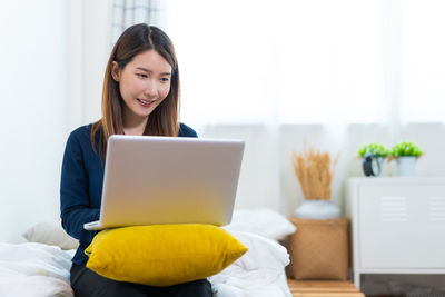 Young woman using laptop while sitting on bed at home