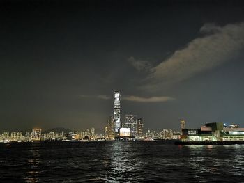 Illuminated buildings by sea against sky at night