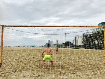 Rear view of men playing soccer on field against sky