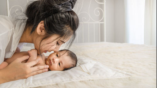 Close-up of woman kissing naked newborn son on bed at home