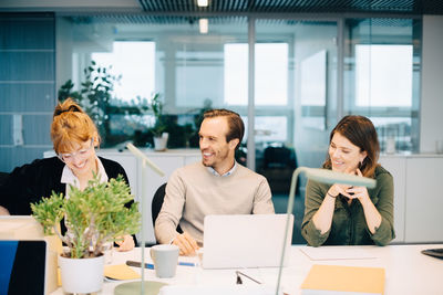 Cheerful business colleagues discussing while sitting at desk in creative office