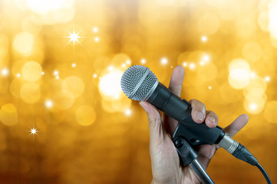 Close-up of cropped hand holding microphone against illuminated lights