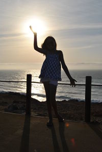 Silhouette woman standing by sea against sky during sunset