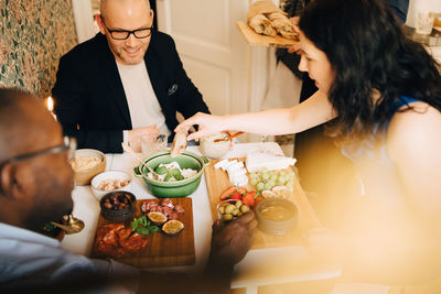 Woman sitting with male friends while having dinner during party at home