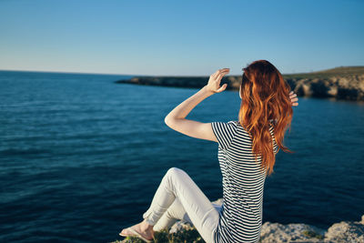 Woman sitting near sea against sky