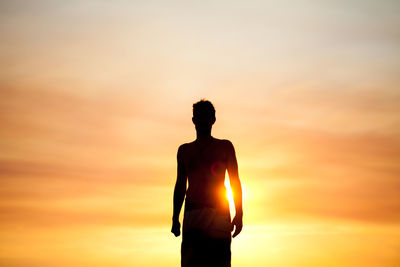 Low angle view of shirtless man standing against sky during sunset
