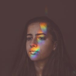 Cute girl with rainbow on face standing against colored background