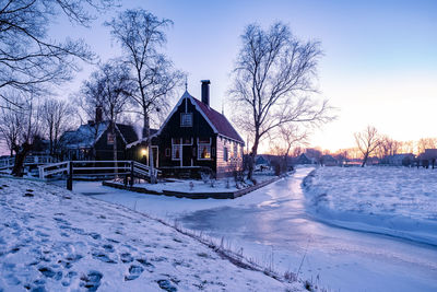 Snow covered houses by building against sky during winter