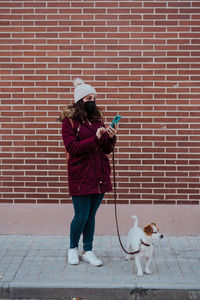 Woman with dog using phone while standing against brick wall