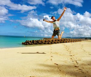 Full length of man with arms outstretched jumping at beach against sky