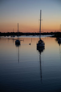 Sailboats moored in lake against sky during sunset