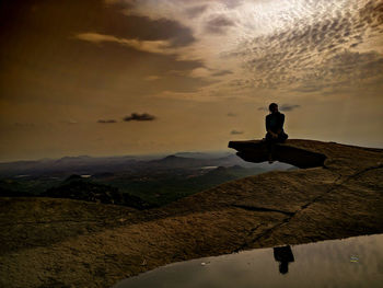 Woman sitting on avalabetta hilltop against sky during sunset