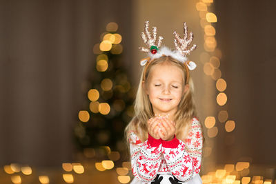 Cute blonde girl 5 years old, sitting near christmas tree and holding garland 