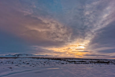 Snow covered landscape against cloudy sky during sunset